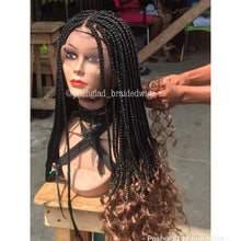 Load image into Gallery viewer, Mannequin head with braided wig on a wooden stand, with a blurred background of people and chairs.